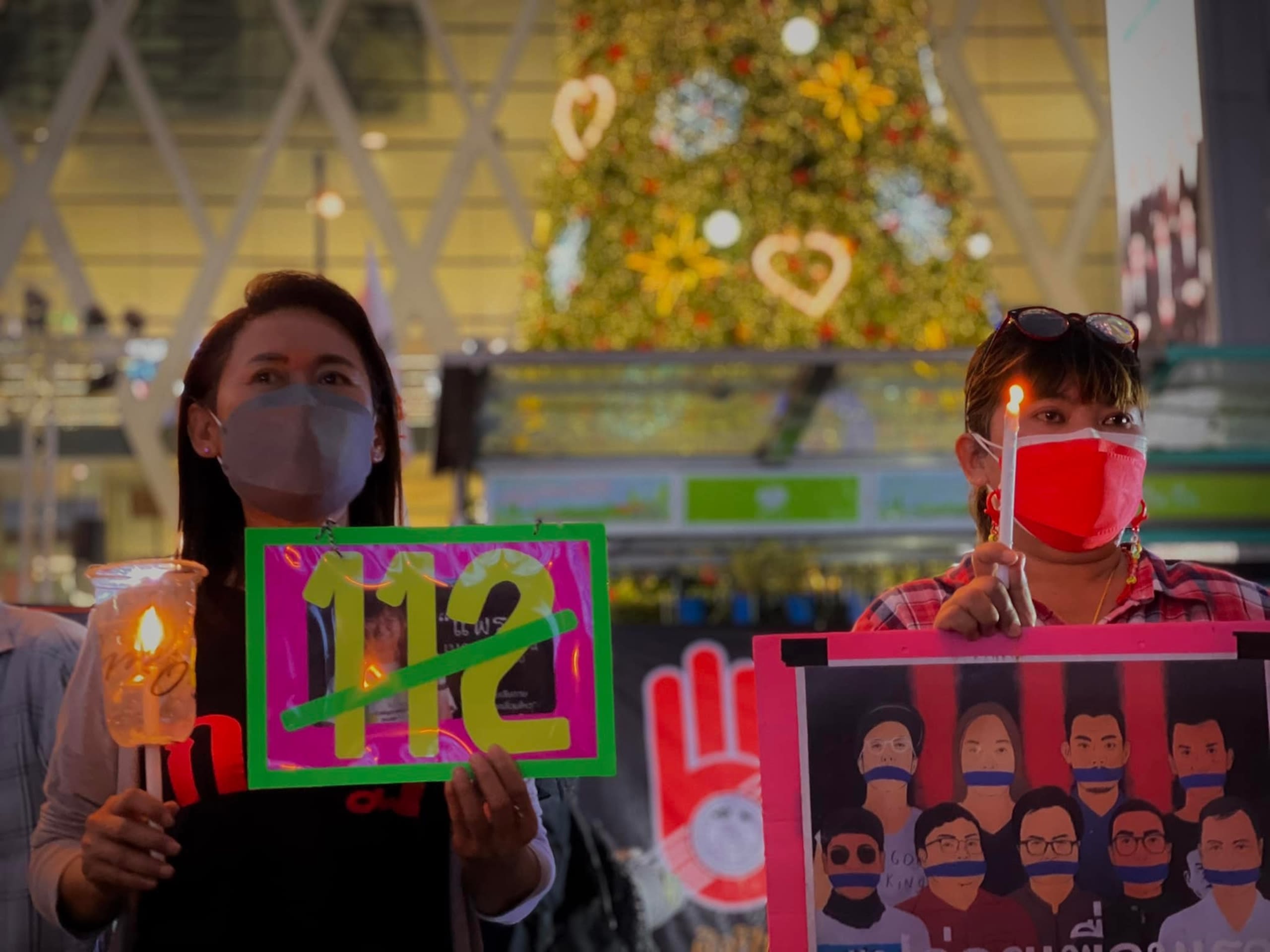 Two women wearing face masks and carrying candles and protest signs. 