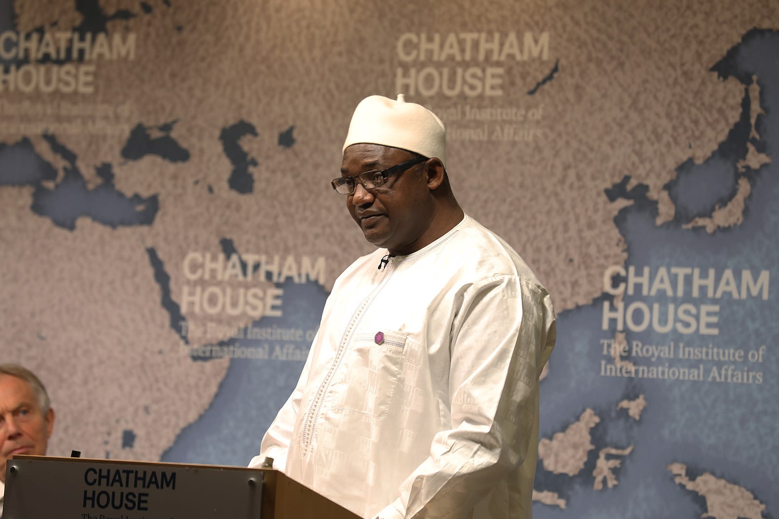 Adama Barrow, President of the Gambia, pictured wearing white and standing in front of a banner depicting a map of the world and the Chatham House logo.
