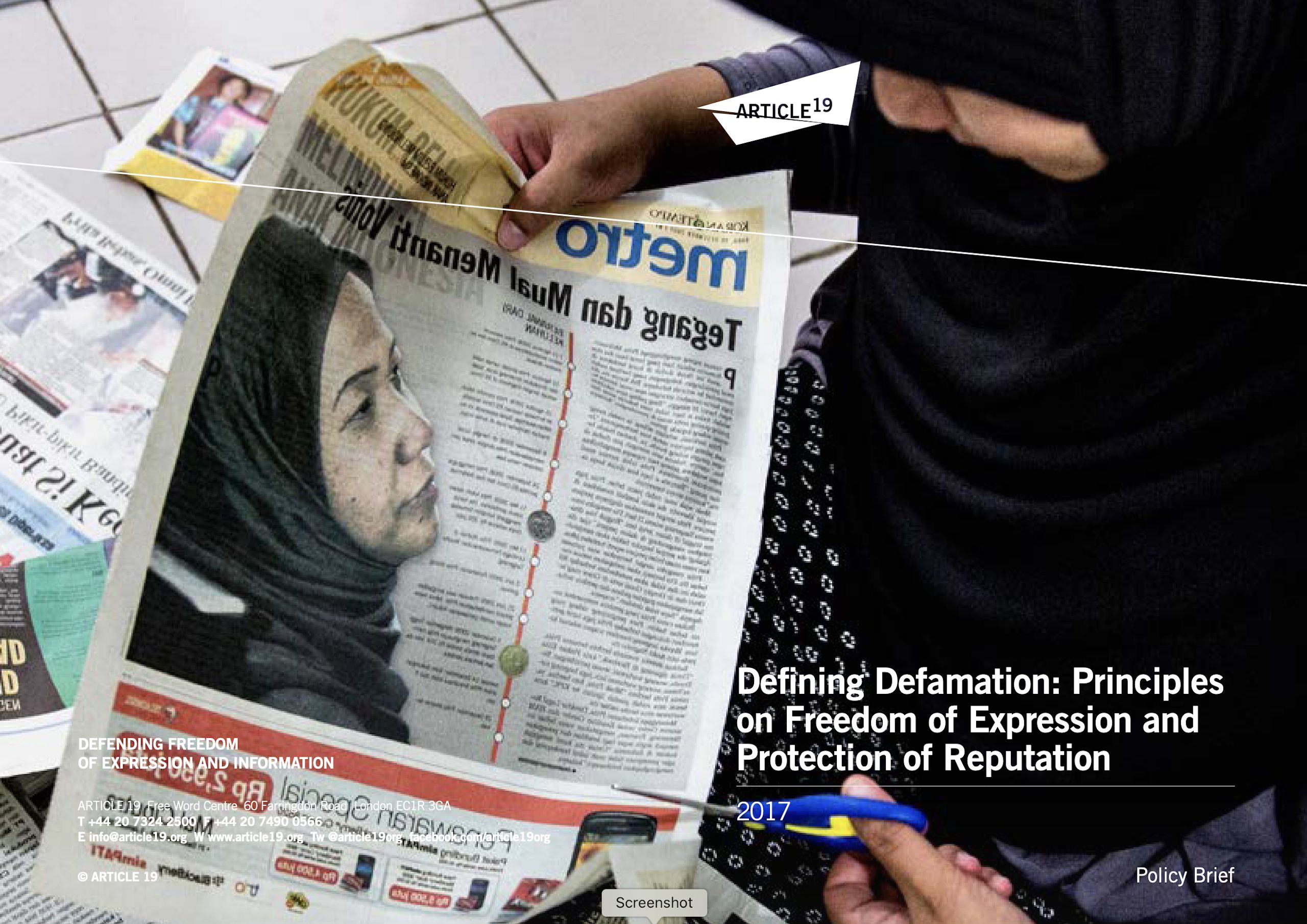 Front cover of ARTICLE 19's publication 'Defining Defamation'. It shows the report title and someone holding a newspaper. The newspaper features a photo of a woman in a black headscarf.