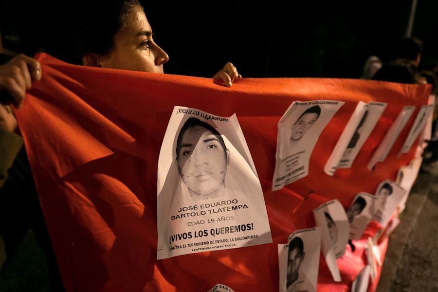 Young woman holds a red banner featuring black-and-white posters of men's faces, each featuring Spanish text.