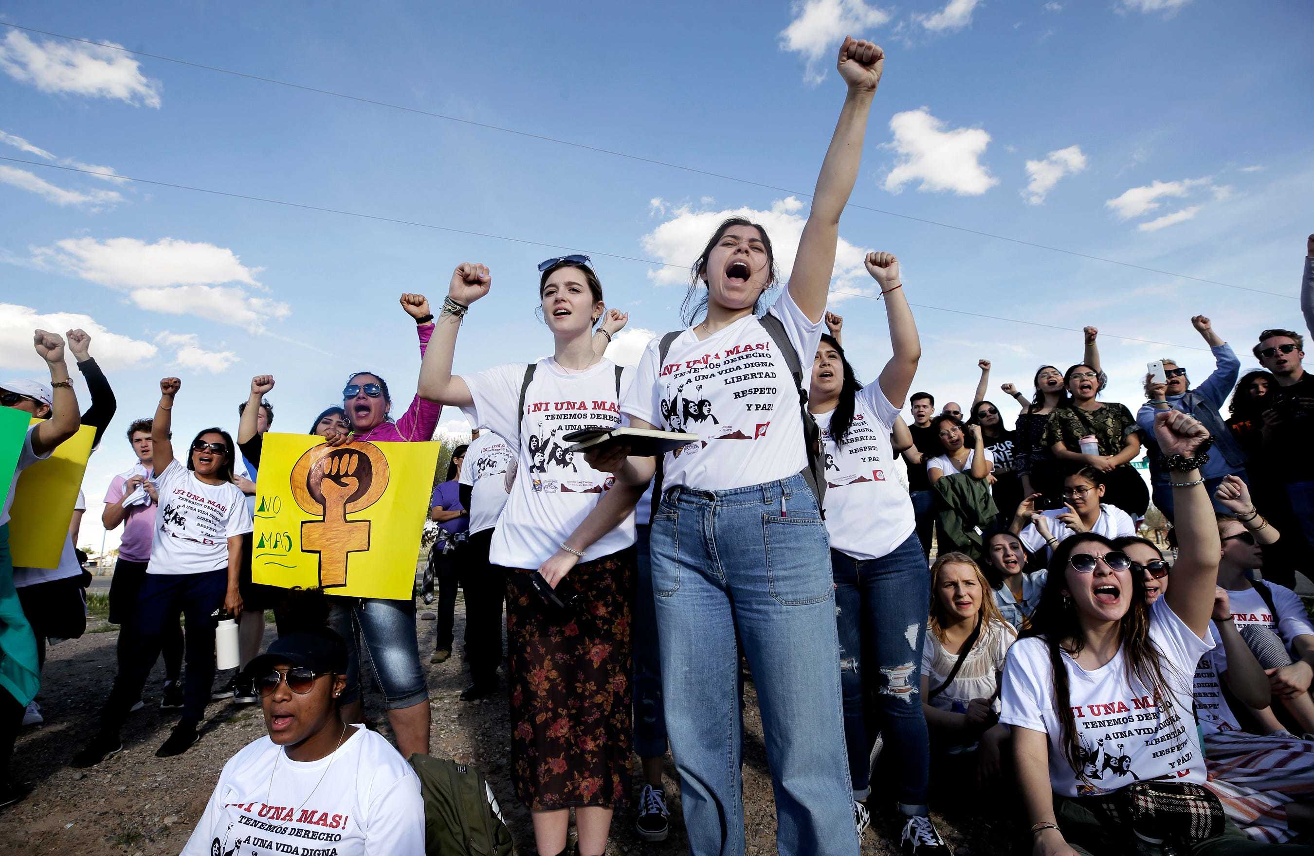 Group of mostly women wearing T-shirts that read 'Ni Una Mas'. One is holding a yellow sign with the female empowerment image on it. They are raising their fists.